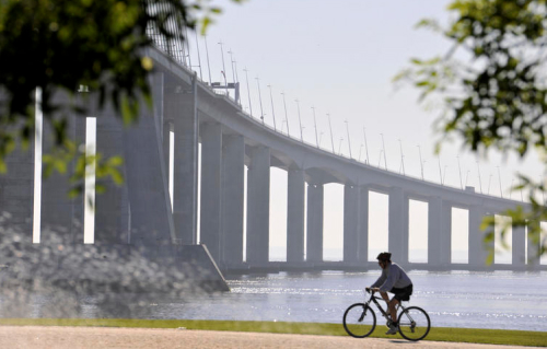 Photo d'une personne se baladant à vélo sur un chemin qui longe la mer avec un pont en fond.