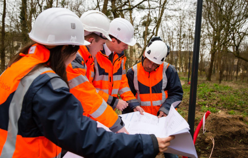 Photo d'une équipe de collaborateurs, avec équipements de sécurité, analysant un plan de chantier.