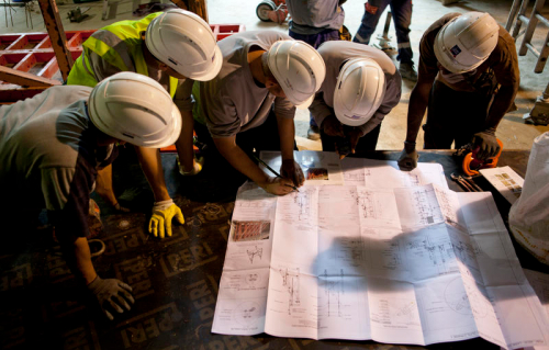 Photo d'une équipe de collaborateurs, avec équipements de sécurité, analysant un plan de chantier.